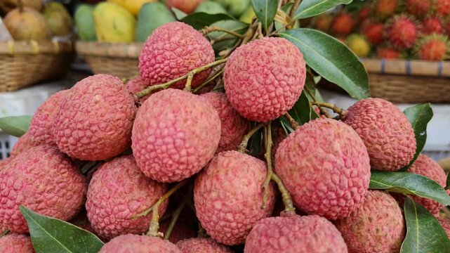Close Up Of Fresh Pink Lychees With Green Leaves Displayed At A Market With Other Fruits In The Background Natural Lighting Creates A