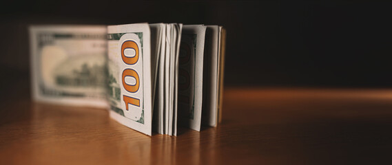 A pile of paper money: American dollars in denominations of $100 and $100 bills. A stack of crumpled bills on a wooden oak table, close-up, blurred, with selective focus. banner closeup copy space
