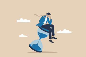 A thoughtful businessman observes time passing while sitting on a large blue hourglass