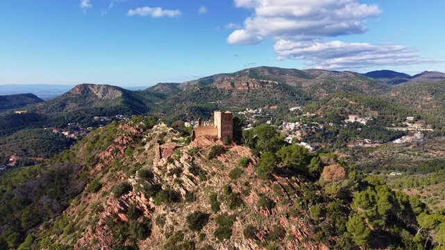 Orbit aerial shot circling the ruins of an ancient hilltop castle near Serra village in the Sierra Calderona Natural Park, Valencia, Spain, with mountains, forests, and dramatic clouds