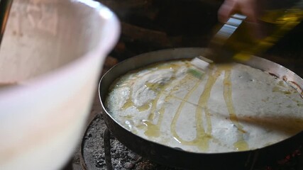 Traditional Cooking Process of Pouring Golden Olive Oil onto Raw Dough in a Metal Tray over Rustic Fire in Zagori Albania