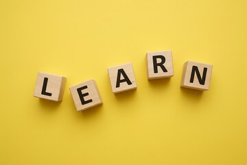 Wooden blocks spelling LEARN, loosely arranged, bright yellow background, minimal personal growth concept