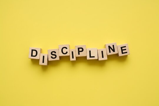 Wooden blocks spelling DISCIPLINE, loosely arranged on  bright yellow background, minimal leadership concept photography.