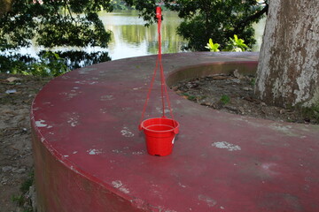 Red Plastic Hanging Pot on Concrete Bench by Water