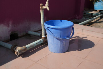 Blue Bucket Under a Rusty Water Tap on a Tiled Rooftop