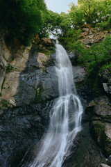 Fototapeta premium majestic waterfall cascading down rocky cliffs surrounded by lush green trees under natural daylight in a serene forest setting