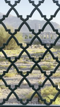 Serene view through an Islamic geometric metal fence revealing an old graveyard, greenery, and distant mountains, blending sacred architecture, history, and calm natural surroundings.