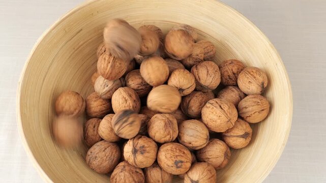 Top-down view of unshelled walnuts being poured into a natural bamboo bowl.