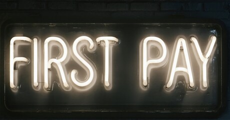 Bright neon sign displays words First Pay. Dark background emphasizes glowing text. Simple, modern aesthetic.