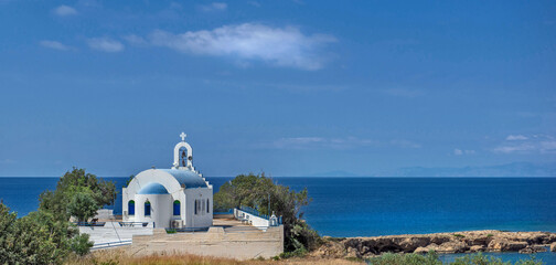 Christian orthodox church with white wall and blue dome at the edge of the blue sea in Peloponnese Greece