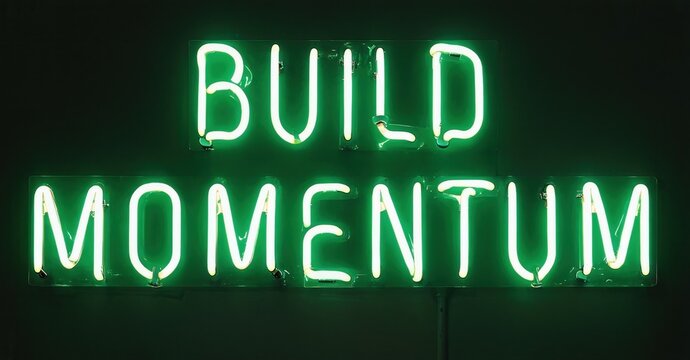 Bright green neon sign displays words build momentum. Dark background emphasizes glowing text. Simple, motivational message presented visually. - Powered by Adobe