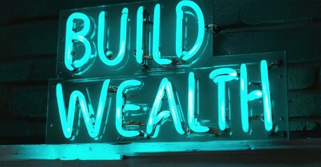 Obraz premium Bright neon sign displays Build Wealth. Dark brick wall provides backdrop. Turquoise glow dominates image. Simple, motivational message.