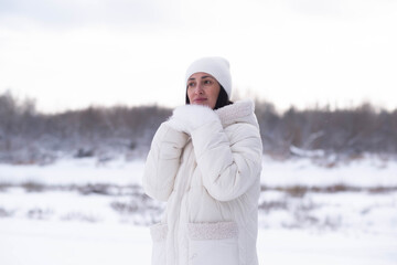 Serene woman in white winter coat and mittens enjoying a snowy day. High-key portrait of seasonal wellness and cozy fashion in a blurred winter landscape.