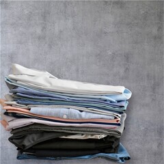 A stack of clean, neatly folded clothes arranged on a light background, representing laundry, wardrobe organization, minimal lifestyle, and household cleanliness