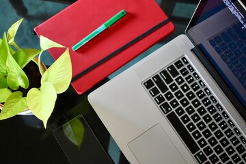 Minimal modern workspace with laptop, red notebook, pen and green plant on glass desk, showing productivity, remote work and creative office lifestyle.