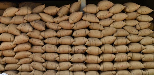 Large burlap sacks stacked in a warehouse storing agricultural produce, representing logistics, supply chain, farming economy, and food storage.