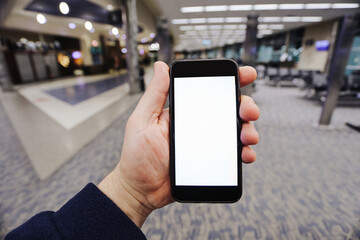 Mobile phone with blank screen at airport terminal. Hand holding smartphone in departure hall. Empty display for travel app interface. Passenger using device while waiting for flight.