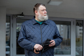 Middle aged man holding umbrella near apartment entrance, rainy urban environment and casual city lifestyle