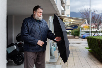 Middle aged man opening umbrella on city sidewalk in rainy weather, casual urban lifestyle scene