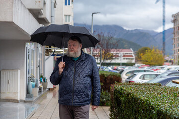 Man walking with umbrella along residential street during rain, calm urban lifestyle and weather concept