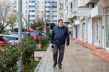 Middle aged man walking along residential sidewalk in city, calm everyday urban lifestyle