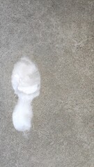 Snowy shoe print on concrete surface. A white snow resembling a footprint contrasts against a rough concrete surface. The texture of the concrete adds depth and interest to the composition.
