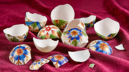 A still life with fragments of painted eggs on dark red velvet fabric. The shells are decorated with bright blue flowers and folk-style patterns. A metaphor for the end of a holiday, the fragility of 