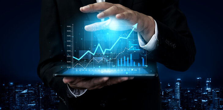 A businessman in a suit interacts with an illuminated digital financial graph on a tablet, showcasing data analytics against a dark city skyline, symbolizing future investments. Scalp - Powered by Adobe
