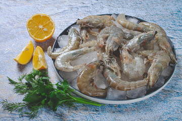 Fresh raw shrimp spread on ice with lemon and cilantro slices on a marble surface, ready to cook, no people