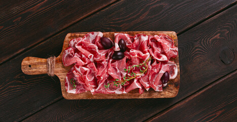 Freshly cut dried meat, served with olives and herbs, on a wooden chopping board, no people,