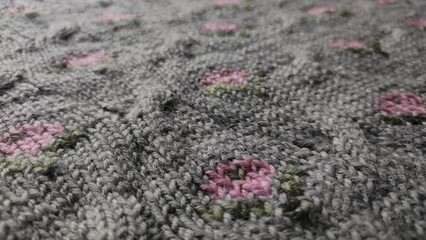 The image showcases a knitted fabric with patterns featuring pink and green floral designs. The texture of the yarn and the detailed stitching are clearly visible, providing a warm and homely feel.