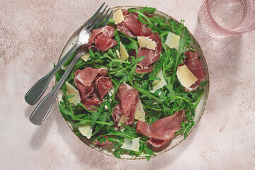 Fresh arugula salad with prosciutto and grated parmesan cheese, on a plate, homemade, no people,