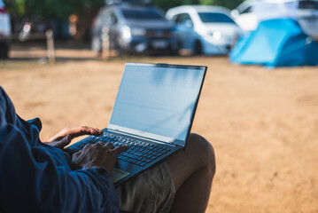 Close-up of a man using a laptop at a campsite. Concept of digital nomad, remote work, and enjoying a vacation in nature.
