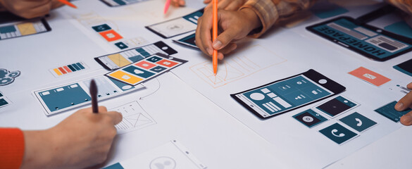 A dynamic team engages in a collaborative UI design session, sketching mobile application layouts with colorful markers on a bright work surface, fostering creativity. SACTR