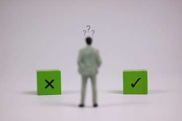 A tiny figurine stands between two green blocks marked X and a check, symbolizing choice, uncertainty, and evaluating options in business or personal decisions. isolated on white background