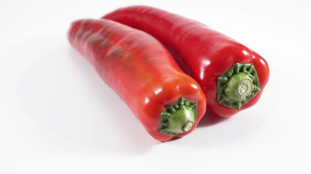 Two elongated red chili peppers rotate under studio lighting against a white background. High-quality stock video that highlights form, color, and freshness.