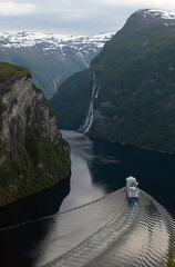 A cruise ship sailing through Geirangerfjord, Norway, surrounded by towering cliffs, waterfalls. Iconic Scandinavian fjord landscape showcasing dramatic nature and adventure travel.
