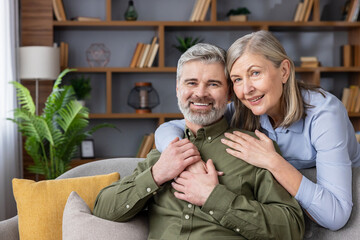 Happy senior couple smiling and experiencing domestic bliss while embracing on a comfortable sofa, representing love, companionship, and a fulfilling life after retirement