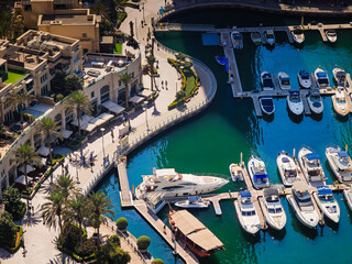 Aerial drone view of Dubai Marina harbor with many luxury yachts, capturing modern waterfront and city skyline. Floating boats on canal