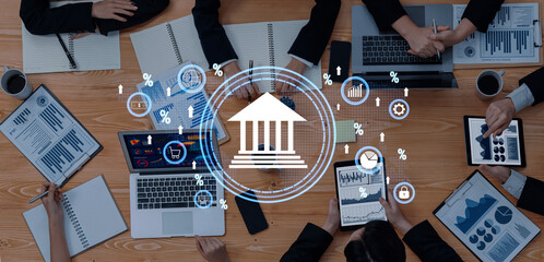 A diverse group of business professionals collaborates on financial analysis using laptops and tablets, with charts and data visualizations on the table. Trope