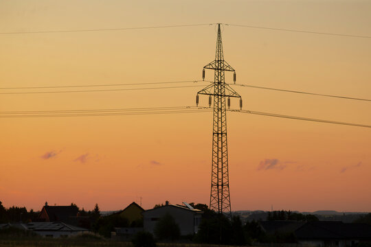 sunset over rural field with pylon, utility technician imagined inspecting transmission lines, warm orange sky, long cables stretching to horizon, distant houses and calm meadow, - Powered by Adobe
