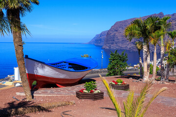 Boat and palm trees at viewpoint Mirador Archipenque in front of vertical cliffs of the Giants (Acantilados de Los Gigantes) and Atlantic Ocean at Canary Island Tenerife, Spain