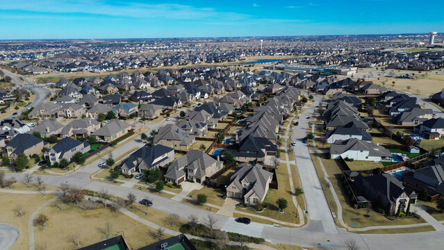 Tennis courts near row of suburban homes and central park with circular amphitheater, school playground. Curved streets, ornamental grasses show layered community planning in Prosper, Texas