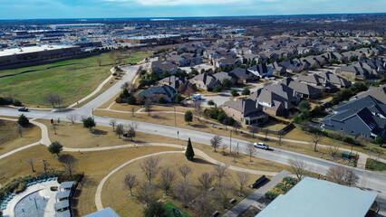 Central park with splash pad, curved walkways, open lawns sits beside residential block in Prosper, TX, nearby commercial buildings emphasizing mixed use convenience and community accessibility