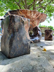 Outdoor decorative table and stools crafted from solid textured stone with unique marble patterns. Durable garden furniture placed in a park setting under the shade of trees