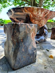 Outdoor decorative table and stools crafted from solid textured stone with unique marble patterns. Durable garden furniture placed in a park setting under the shade of trees