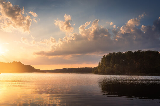 Amazing sunrise over lake with colorful clouds at the horizon. Forest on the lake side. Sunny morning in wild nature.