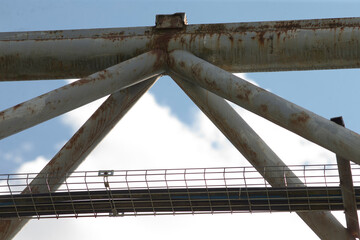 steel truss forming triangular geometry against sky, clean lines and lattice pattern with grated walkway and protective mesh, subtle rust tones suggest aging infrastructure
