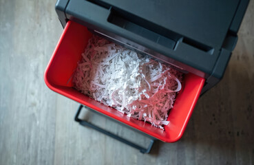 Paper shredder bin filled with shredded paper strips. Machine destroys confidential documents ensuring data privacy and security. Office equipment cleans up sensitive information for safe disposal.