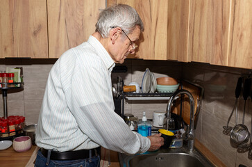 A senior man pours water into a cup from a tap. Filling cup of water from stainless steel kitchen faucet